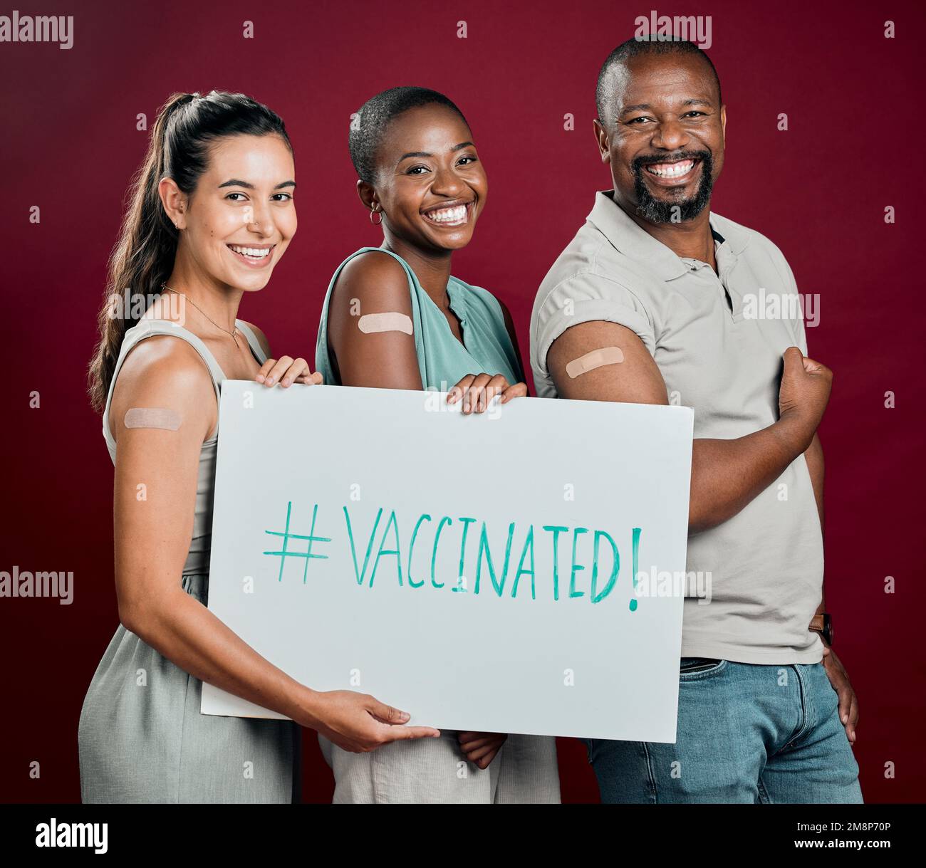 Covid-geimpfte verschiedene Personengruppen, die Poster zeigen und in der Hand halten. afroamerikanischer Mann und Frau mit gemischter Rasse, isoliert auf rotem Atelier Stockfoto