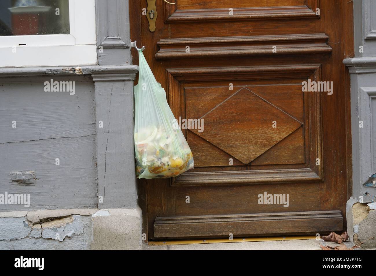 Organischer Abfall in einer Plastiktüte, der an einem Türknauf einer Haustür hängt. Stockfoto