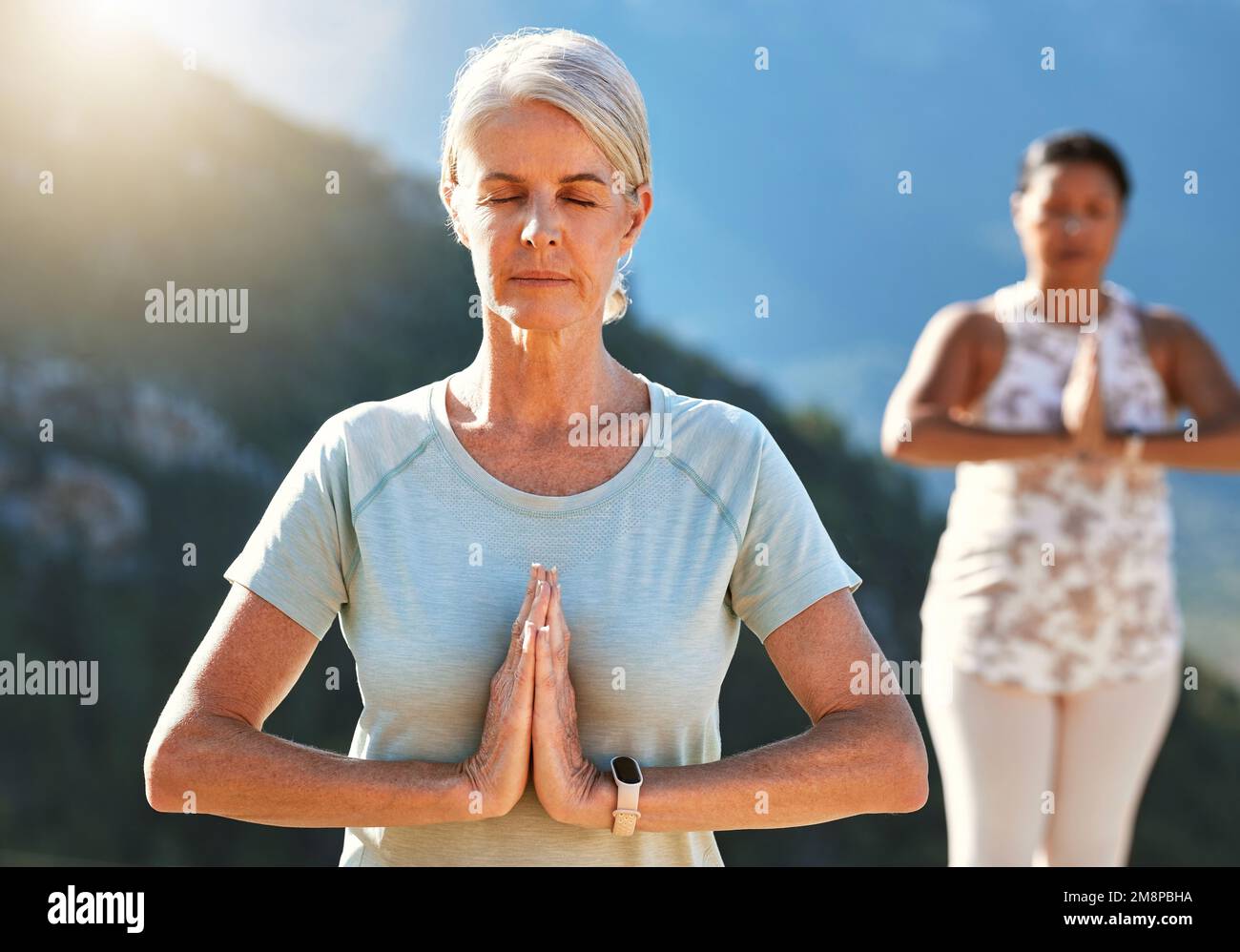 Seniorin meditiert mit verbundenen Händen und geschlossenen Augen tief atmen. Reife Menschen, die gemeinsam Yoga in der Natur an einem sonnigen Tag machen. Ich finde Inneres Stockfoto