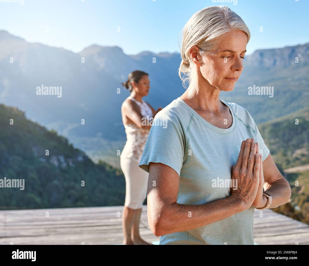 Seniorin meditiert mit verbundenen Händen und geschlossenen Augen tief atmen. Klasse reifer Leute, die zusammen Yoga in der Natur an einem sonnigen Tag machen Stockfoto