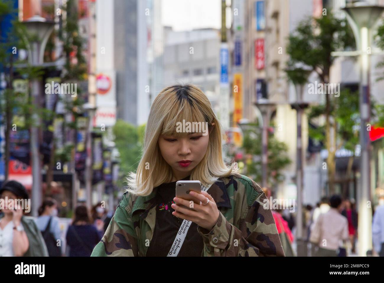 Eine Japanerin mit gefärbtem blondem Haar, die ein iPhone auf der Straße in Ikebukuro, Tokio, Japan benutzt. Stockfoto