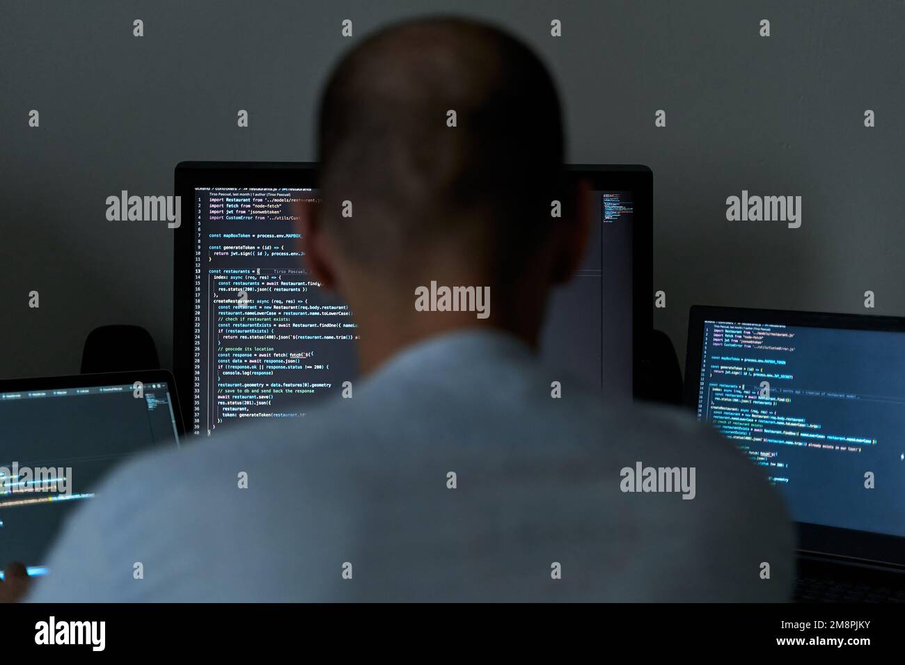 Junger Mann schreibt Codierung auf drei Bildschirmen. Softwareprogrammierer und Webentwickler Stockfoto