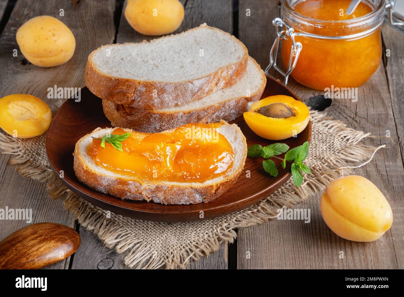 Toasts mit Brot mit Aprikosenmarmelade und frischem Obst mit Minze auf einem Holztisch Stockfoto