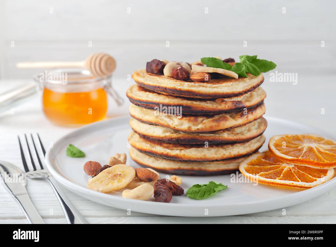 Frische hausgemachte Pfannkuchen mit getrockneten Bananen, Orangen, Nüssen und Honig auf einem Teller. Stockfoto