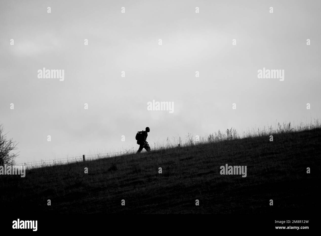 Silhouette eines britischen Infanterie-Soldaten auf einer voll beladenen Lasche, die einen Hügel hinaufmarschiert, Wiltshire UK Stockfoto