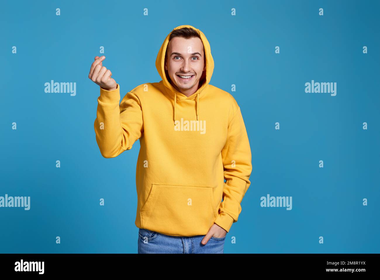 Junger Mann in gelbem Sweatshirt, der eine Liebesgeste zeigt Stockfoto