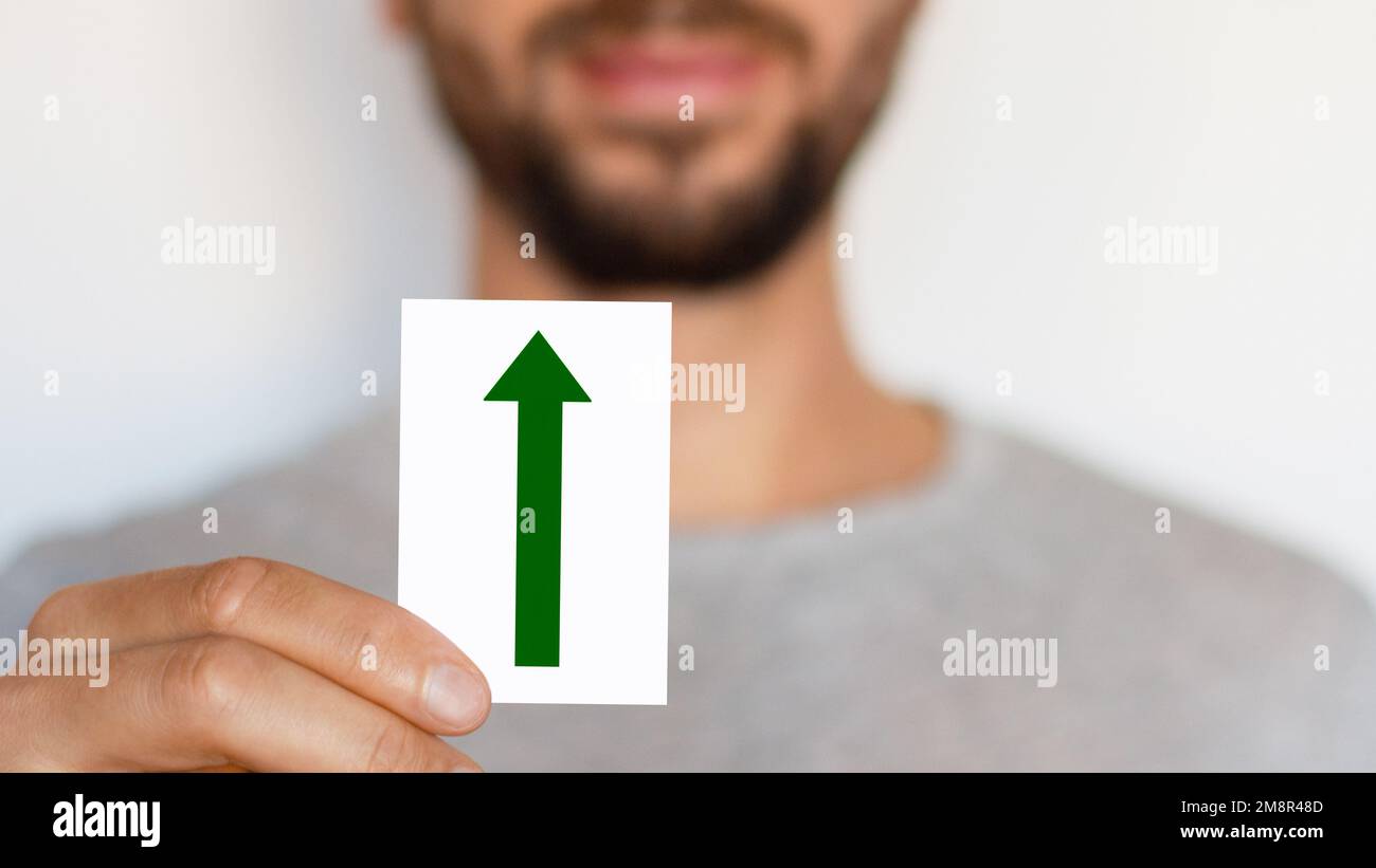 Mann mit Pfeil-Schild. Grüner Pfeil zeigt nach oben. Das Männchen. Richtung. Bewegung. Wo? Wachstum. Stockfoto
