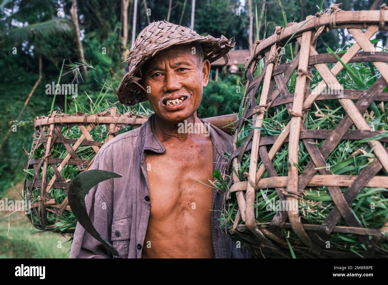 Horizontales Porträt südasiatischer balinesischer Senioren mit traditioneller kegelförmiger Mütze. Älterer Mann mit schiefen Zähnen, der in die Kamera schaut Stockfoto