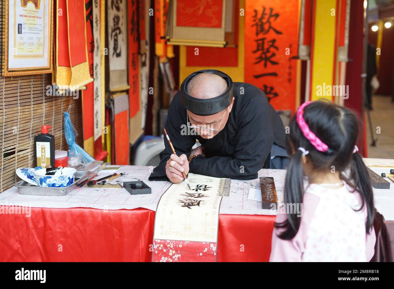 Hanoi, Vietnam. 15. Januar 2023. Ein Kalligraf schreibt ein kalligrafisches Werk für ein Mädchen während des Spring Calligraphy Festivals am Van Mieu-Quoc TU Giam (Literaturtempel) in Hanoi, Vietnam, 15. Januar 2023. Das jährliche Frühjahrskalligrafiefest fand am Sonntag in der vietnamesischen Hauptstadt Hanoi statt, nachdem die COVID-19-Pandemie zwei Jahre zurückliegt. Es ist eine lokale Tradition, kalligraphische Werke auf rotem Papier zu haben, die während des Mondneujahrs ausgestellt werden, um für das gute im neuen Jahr zu beten. Kredit: Hu Jiali/Xinhua/Alamy Live News Stockfoto