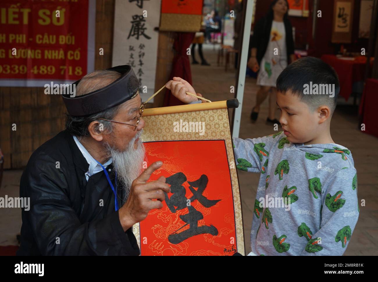 Hanoi, Vietnam. 15. Januar 2023. Ein Kalligraf schreibt ein kalligrafisches Werk für einen Jungen während des Spring Calligraphy Festivals am Van Mieu-Quoc TU Giam (Literaturtempel) in Hanoi, Vietnam, 15. Januar 2023. Das jährliche Frühjahrskalligrafiefest fand am Sonntag in der vietnamesischen Hauptstadt Hanoi statt, nachdem die COVID-19-Pandemie zwei Jahre zurückliegt. Es ist eine lokale Tradition, kalligraphische Werke auf rotem Papier zu haben, die während des Mondneujahrs ausgestellt werden, um für das gute im neuen Jahr zu beten. Kredit: Hu Jiali/Xinhua/Alamy Live News Stockfoto