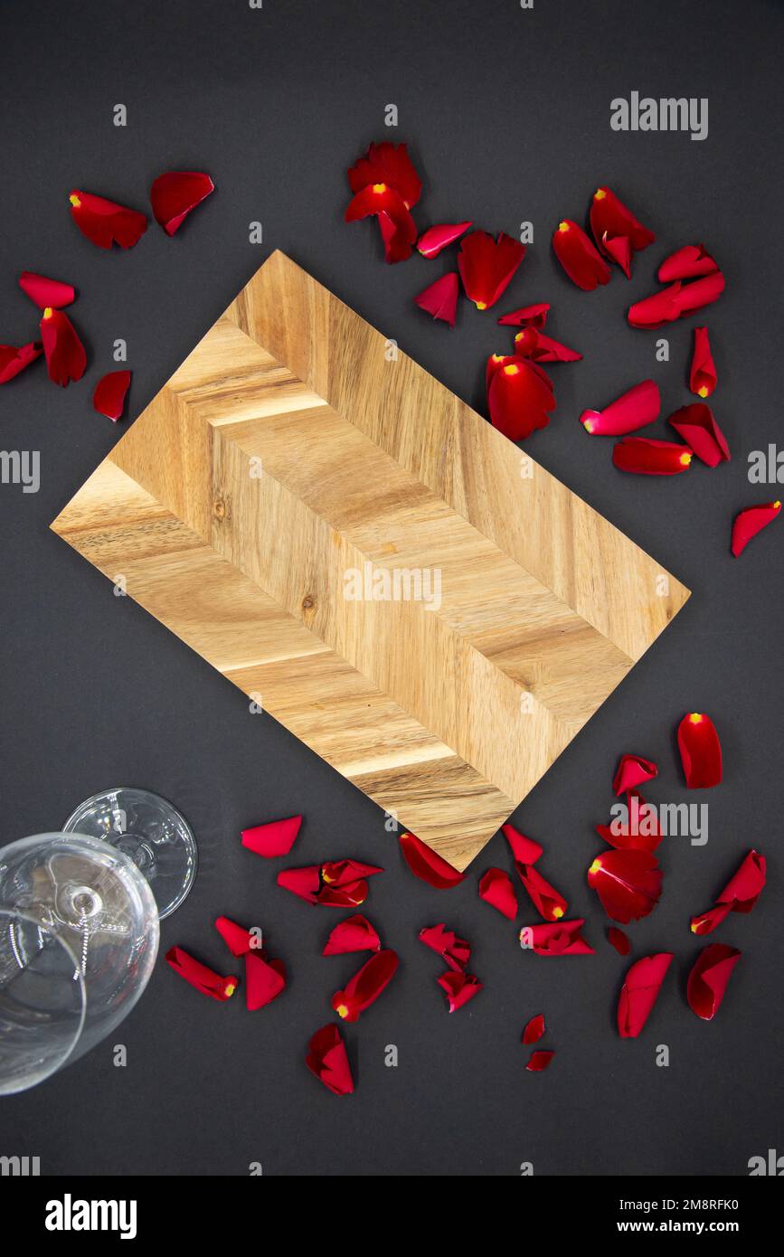 Holzbrett zum Kochen auf dunkelschwarzem Hintergrund mit einem Glas Wein und roten Rosenblättern. Ansicht von oben. Stockfoto