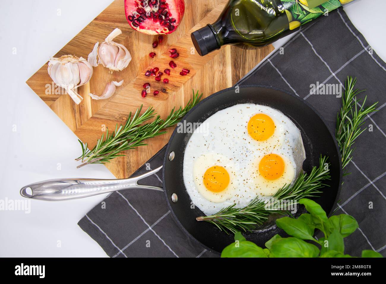 Frühstück oder Brunch, Spiegeleier in schwarzen Pfannen und roter Granatapfel mit Knoblauch und Basilikum. Ansicht von oben. Stockfoto