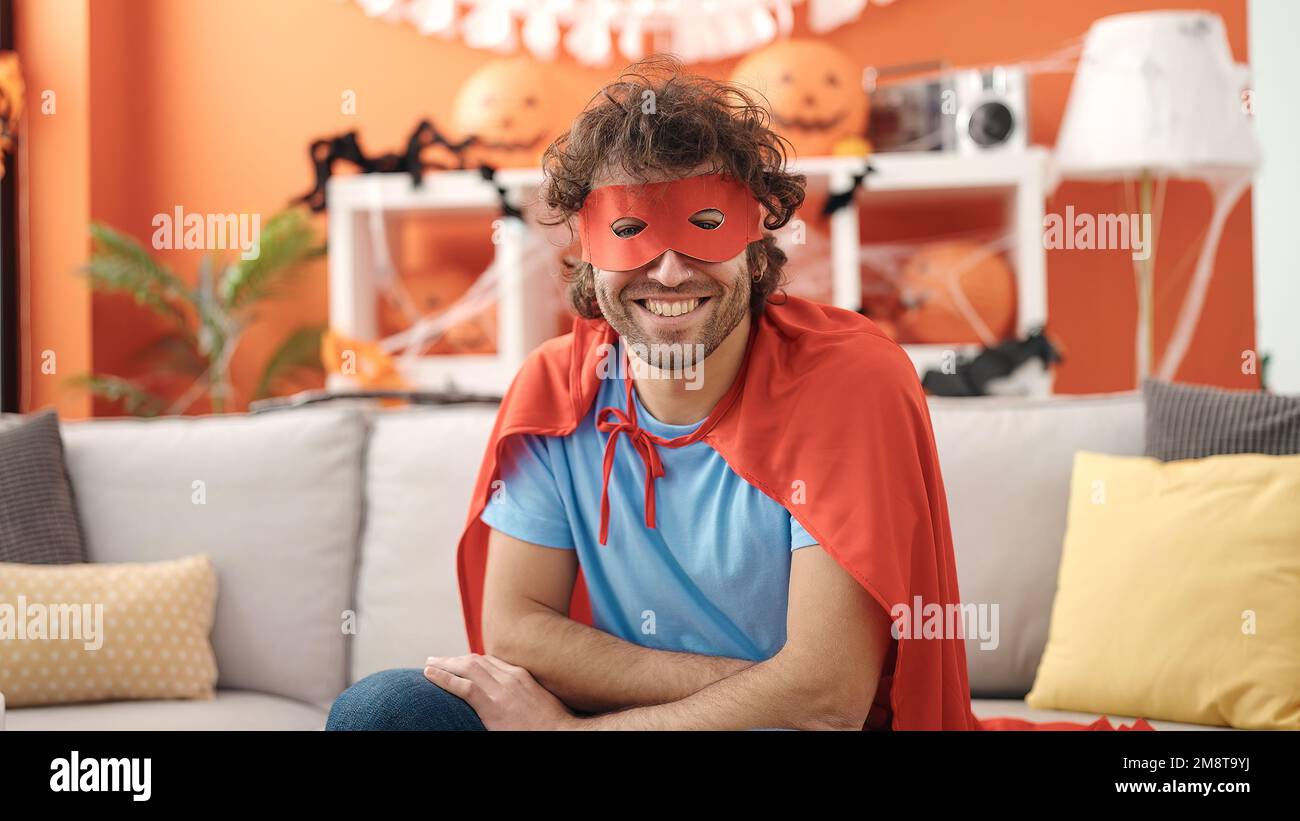 Junger lateinamerikanischer Mann in Superheldenkostüm, der zu Hause halloween-Party macht Stockfoto