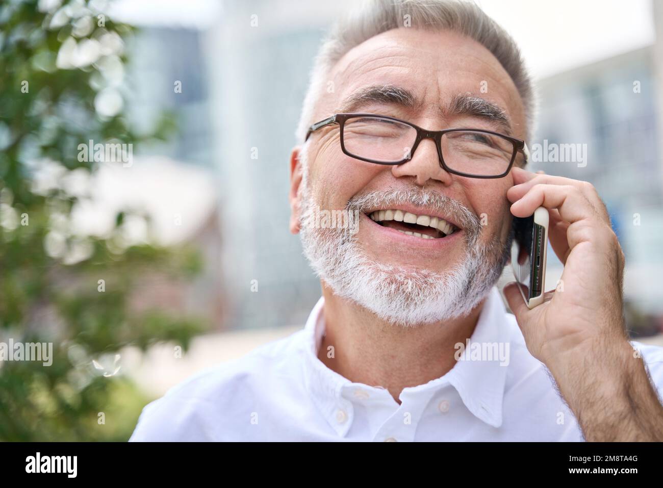 Glücklicher älterer Geschäftsmann, der mit dem Handy telefoniert und draußen in der Stadt telefoniert. Stockfoto