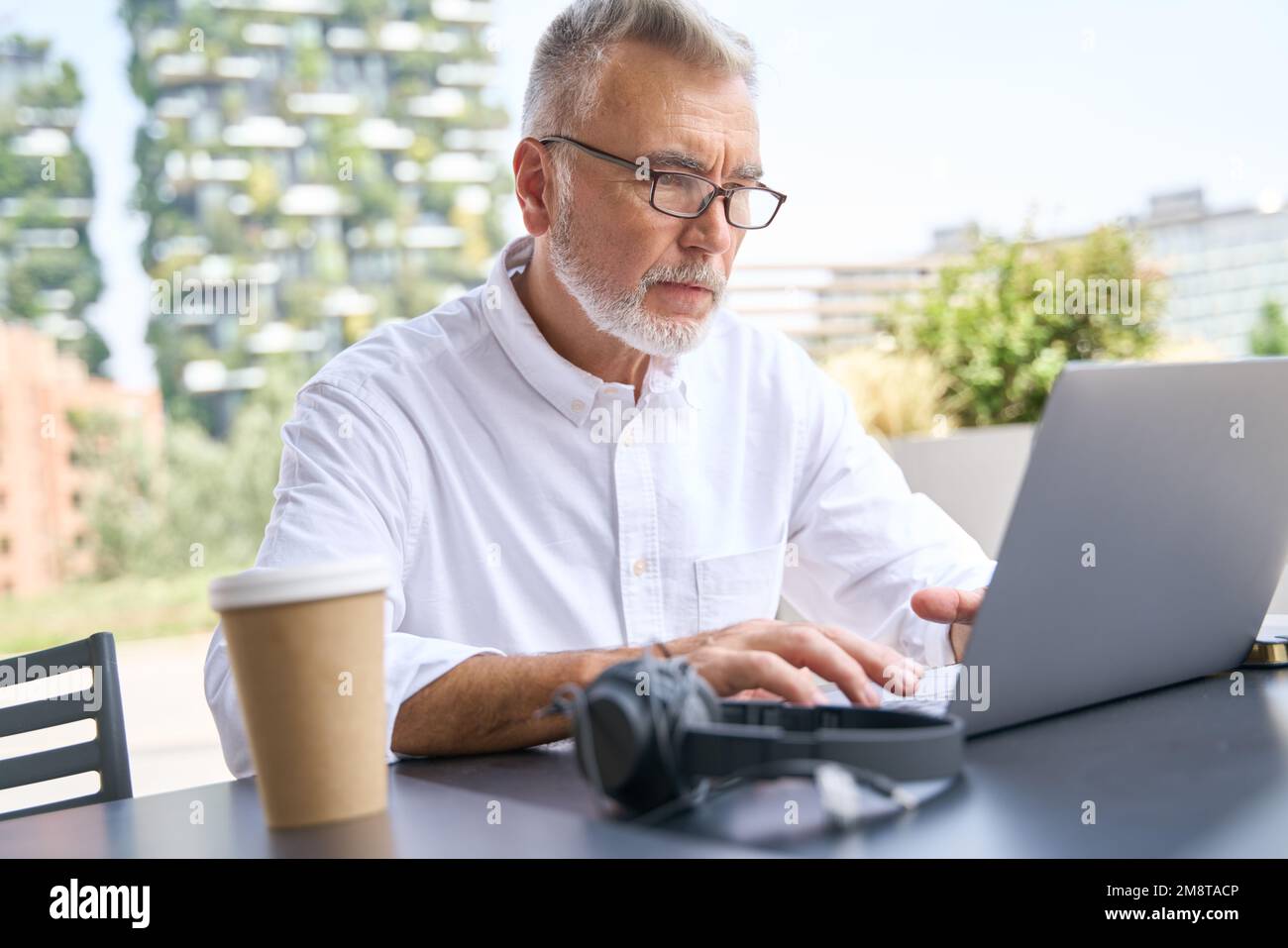 Älterer Geschäftsmann, der im Außenbereich mit Laptop-Computer e-learning arbeitet. Stockfoto