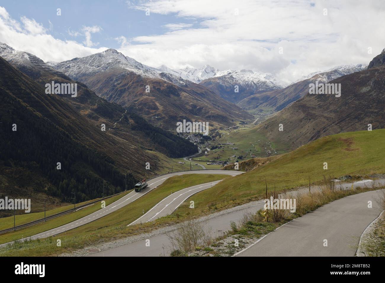 Mit Blick auf ein Tal in den Alpen mit einer Haarnadelstraße und schneebedeckten Bergen in der Ferne, Schweiz Stockfoto