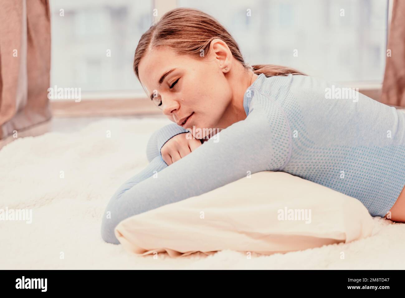 Seitliches Porträt einer entspannten Frau mit langen Haaren, die zu Hause auf dem Teppich lag. Sie trägt einen blauen Trainingsanzug und hält ein Telefon in der Hand. Stockfoto