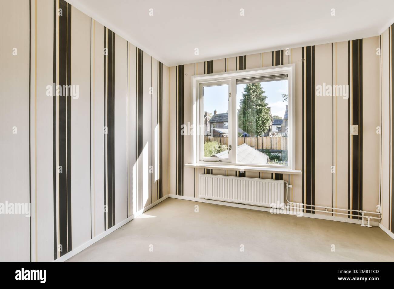 Ein leerer Raum mit gestreiften Tapeten an den Wänden und großen Fenstern im Raum ist weiß, beige und schwarz Stockfoto