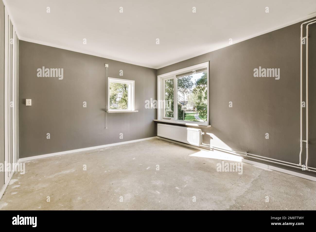 Ein leerer Raum mit grauen Wänden und weißen Verzierungen um die Fensterscheiben auf der linken Seite des Raums Stockfoto