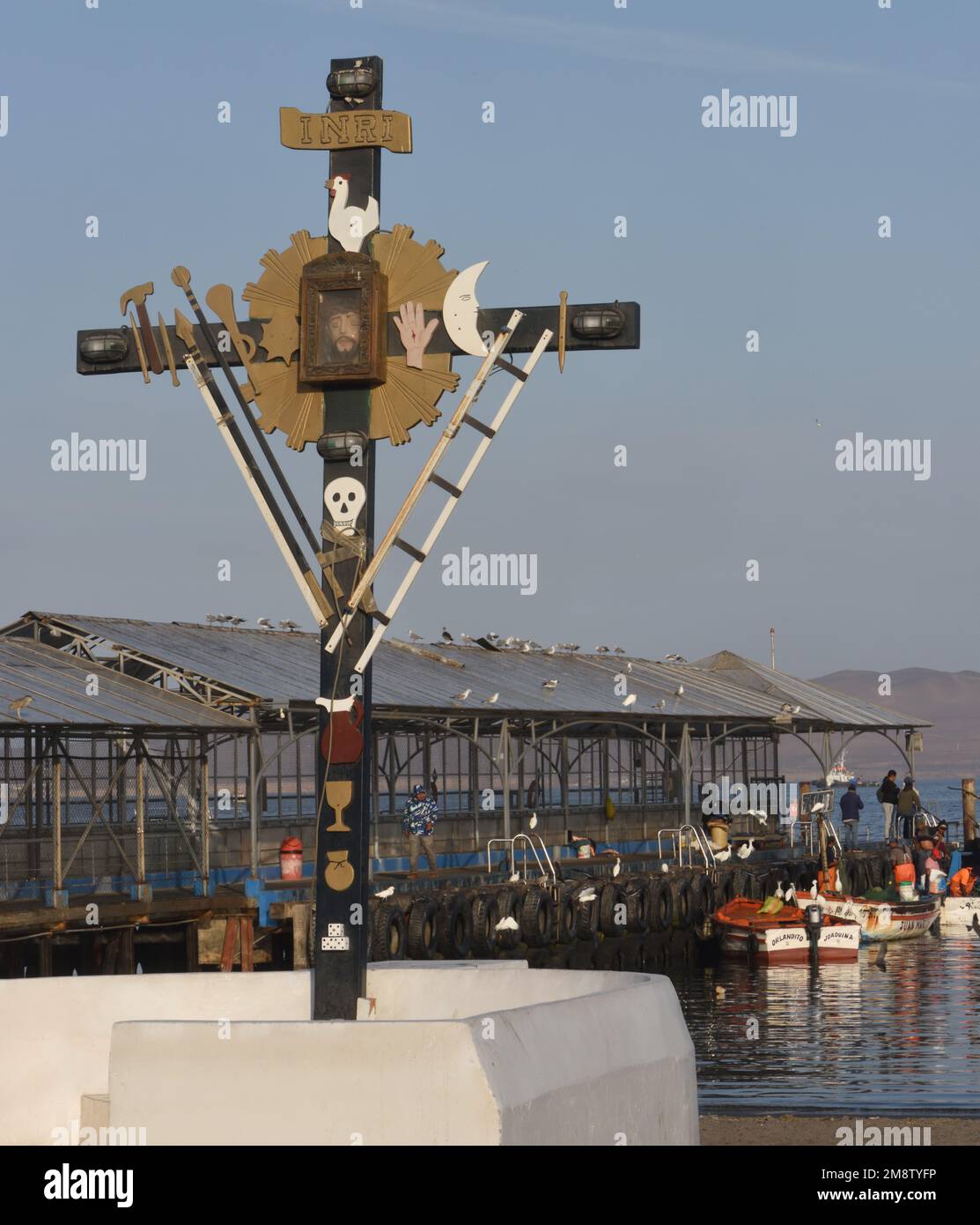 Ein Kreuz mit Darstellungen der Arma Christi, der Waffen Christi oder der Instrumente der Passion, in der Nähe des Fischerboots Pier Paracas. Sym Stockfoto