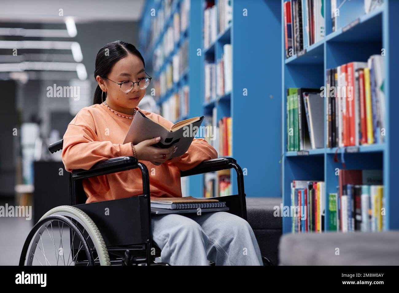 Porträt einer jungen asiatischen Frau mit Behindertenlesebuch in der Bibliothek, Schülereinbeziehungskonzept Stockfoto