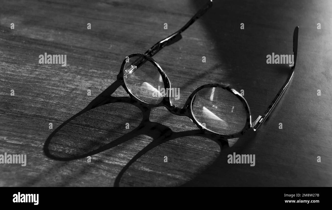 Gläser auf Holztisch. Sonnenschein auf Vintage-Gläsern auf dem Tisch. Weisheitskonzept. Platz für Text kopieren. Schwarz-weiße Hintergrundfarbe Stockfoto