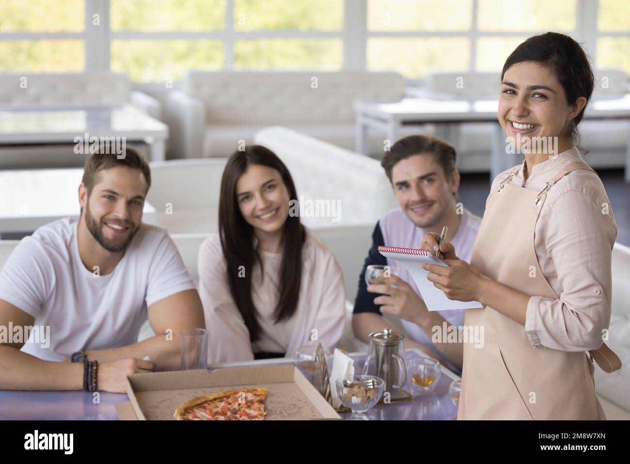 Porträt einer hübschen indischen Kellnerin, die eine Gruppe von Gästen bedient Stockfoto