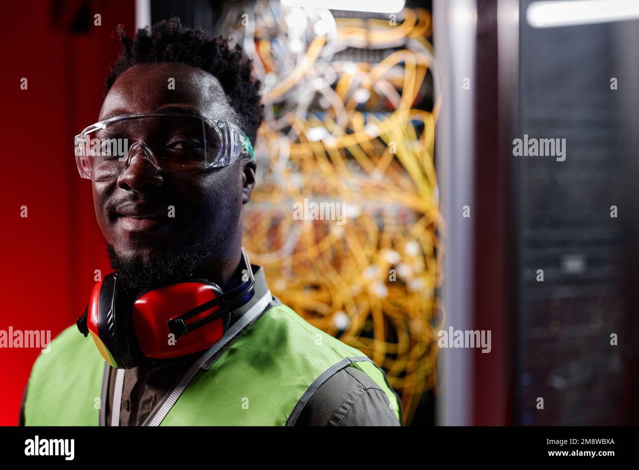 Gesättigtes Porträt eines Schwarzen als Netzwerktechniker, der im Serverraum auf die Kamera schaut, Kopierraum Stockfoto