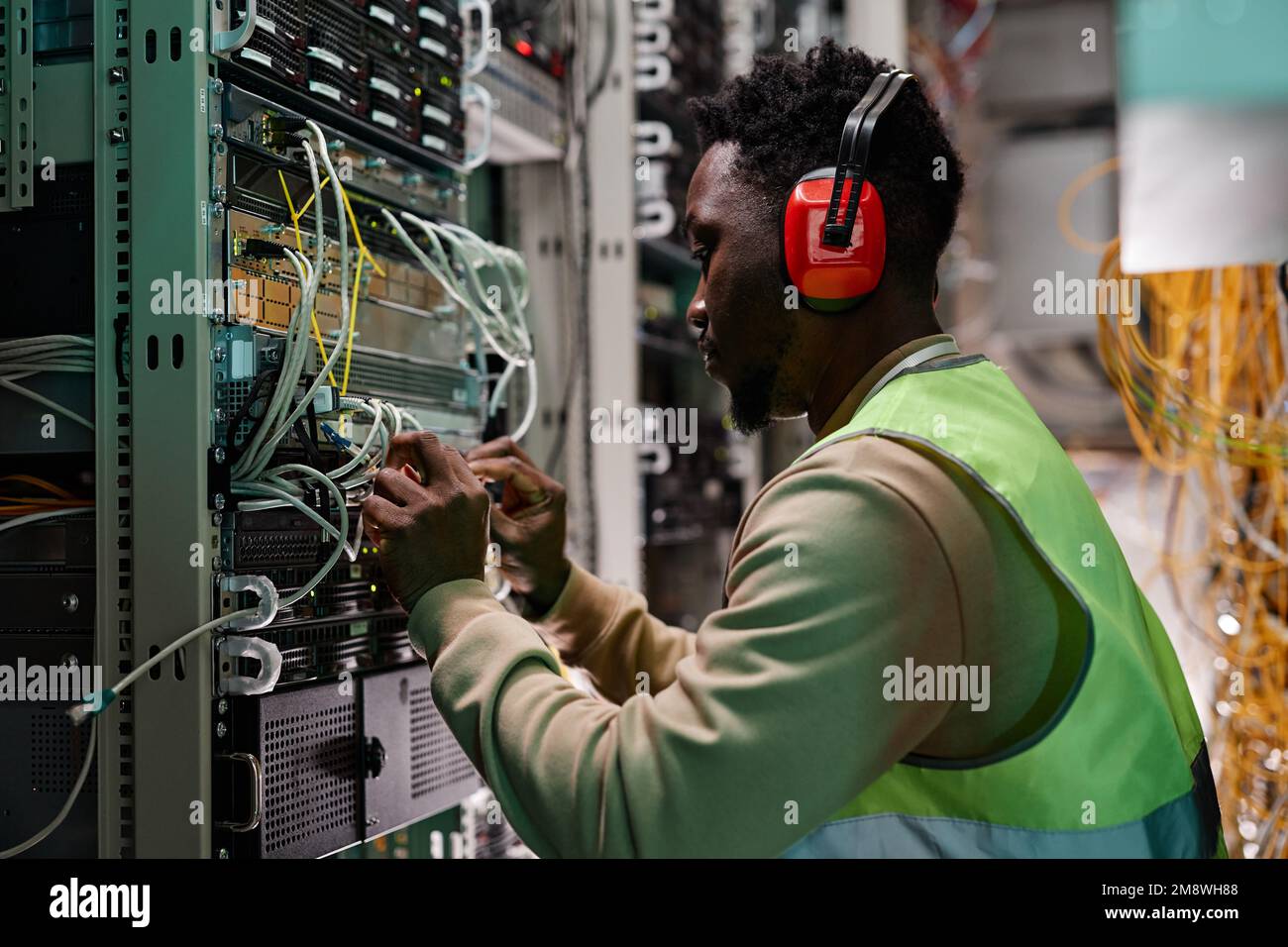 Seitliches Porträt eines jungen Technikers, der ein Netzwerk im Serverraum einrichtet und schützende Arbeitskleidung trägt Stockfoto