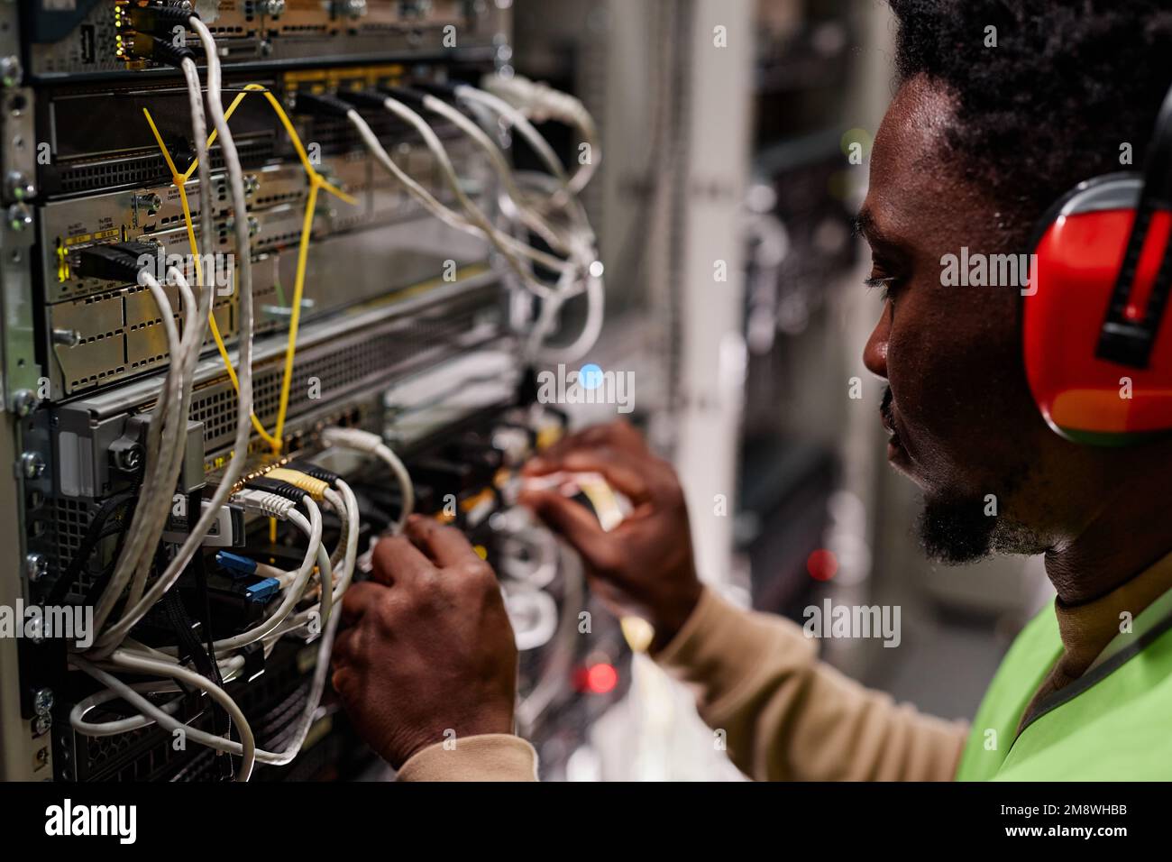 Nahaufnahme des Technikers, der das Netzwerk im Serverraum einrichtet und einen Gehörschutz trägt Stockfoto