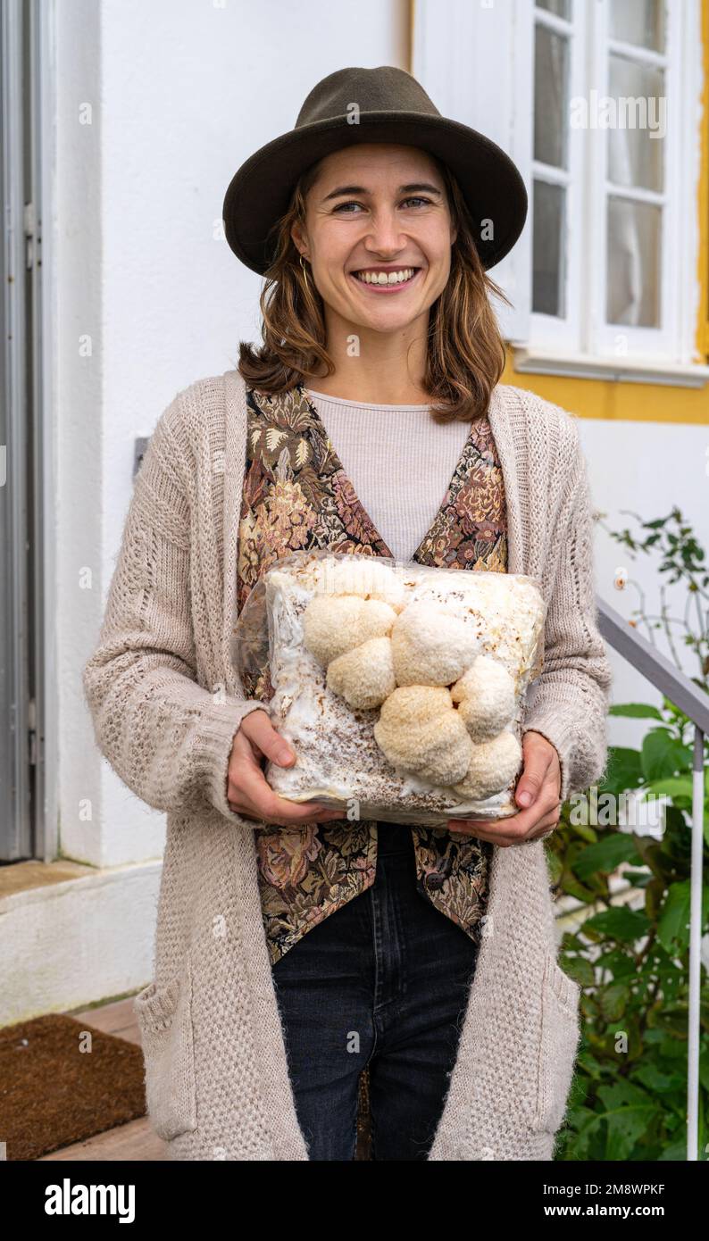 Junge lächelnde Frau, die ein Medium mit Löwenmähnenpilzen hält Stockfoto