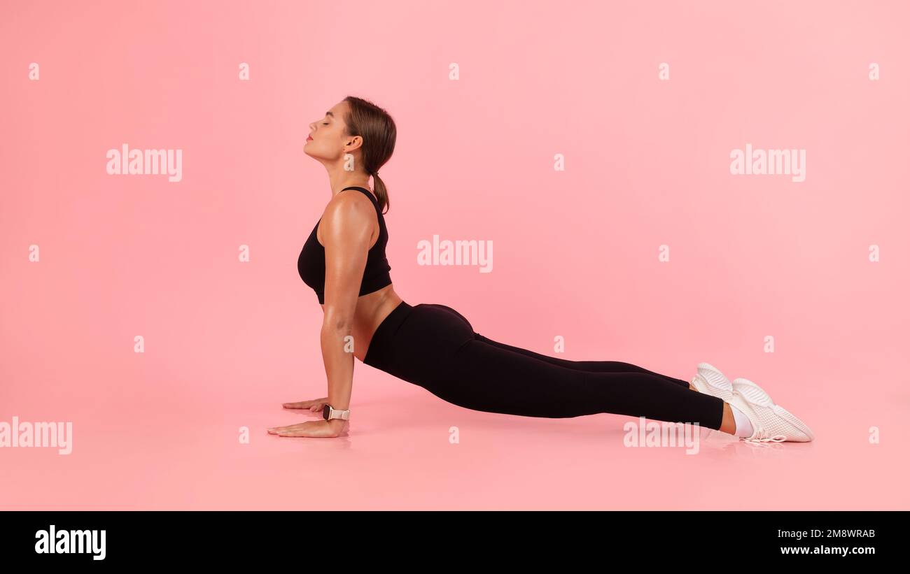 Sportliche junge Frau, die in geschlossenen Räumen Yoga praktiziert und mit dem Hund nach oben schaut Stockfoto