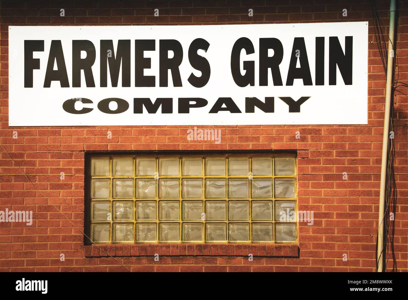 2019 02 08 Wakita Oklahoma USA - Farmers Grain Company-Schild über einem Glasblockfenster in einem Ziegelgebäude mit unordentlichen Drähten Stockfoto