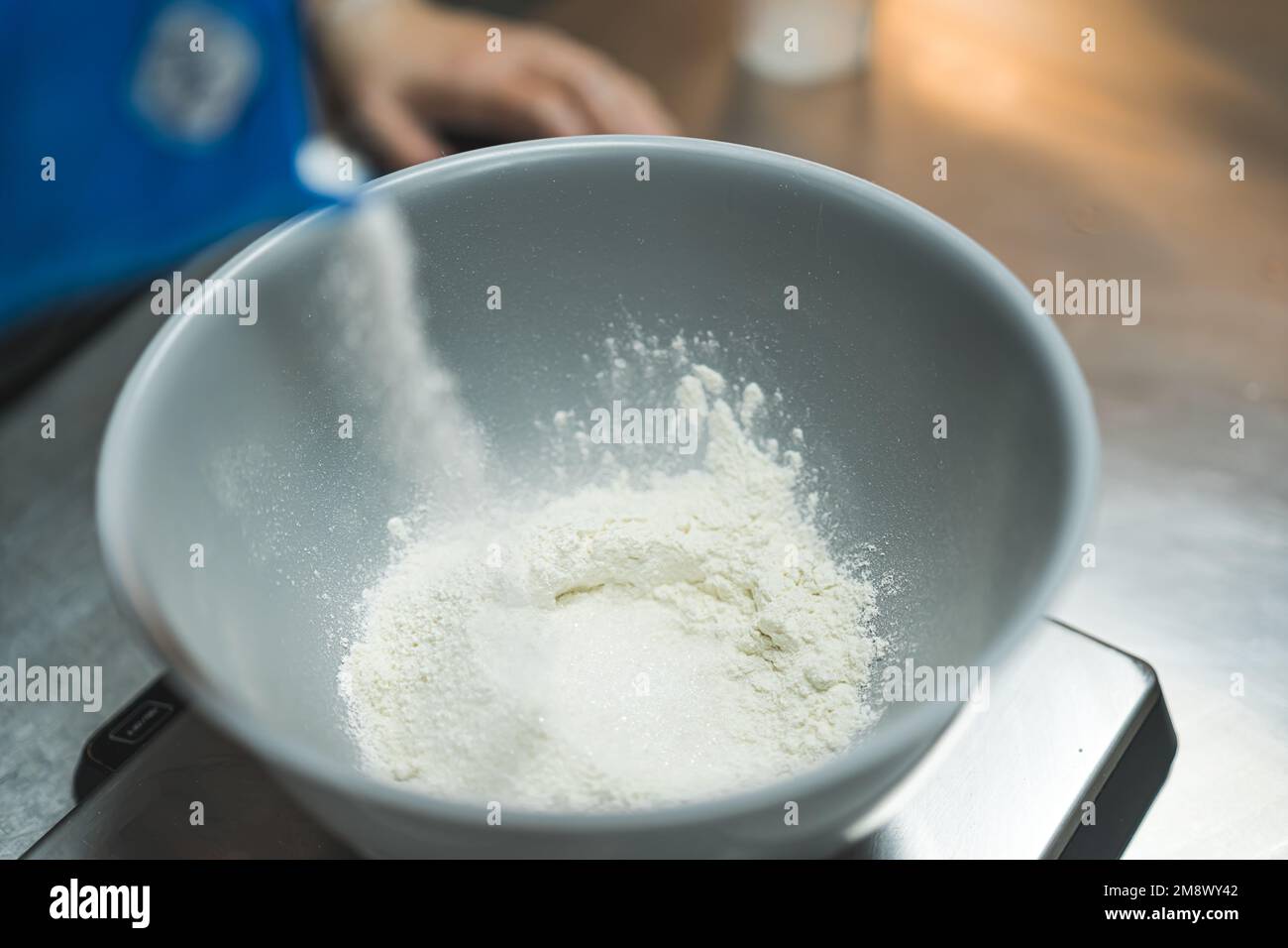 Professioneller Bäcker, der Mehl in eine weiße Schüssel abmisst, um Cupcake-Teig zuzubereiten. Backvorgang. Trockene Zutaten. Horizontale Indoor-Aufnahme. Hochwertiges Foto Stockfoto