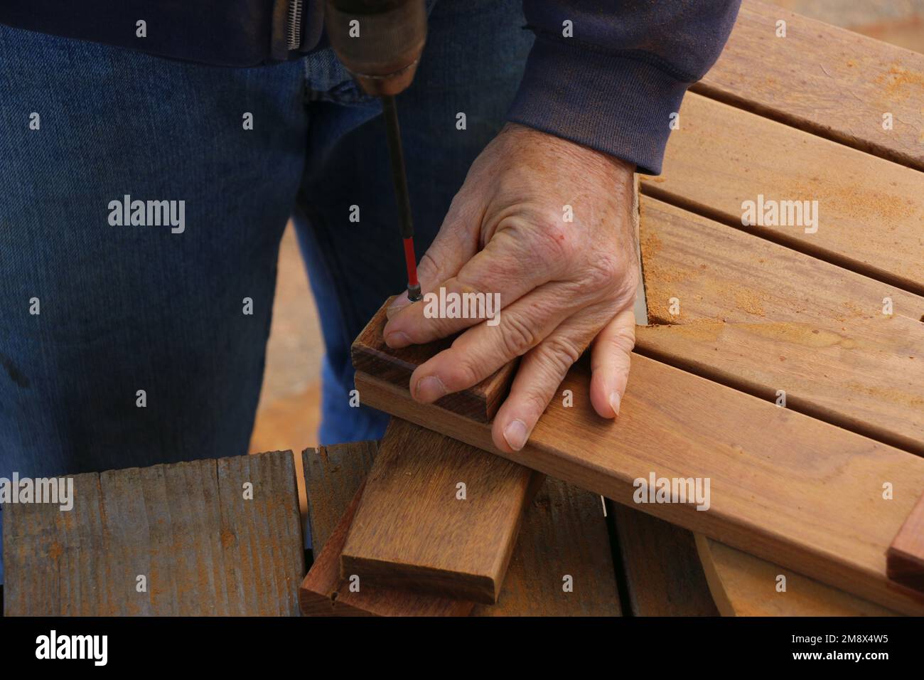 Nahaufnahme der Hände eines Seniors, der einen Bohrer verwendet, um ein Holzbearbeitungsprojekt zum Bau von Bodenbelägen durchzuführen. Stockfoto