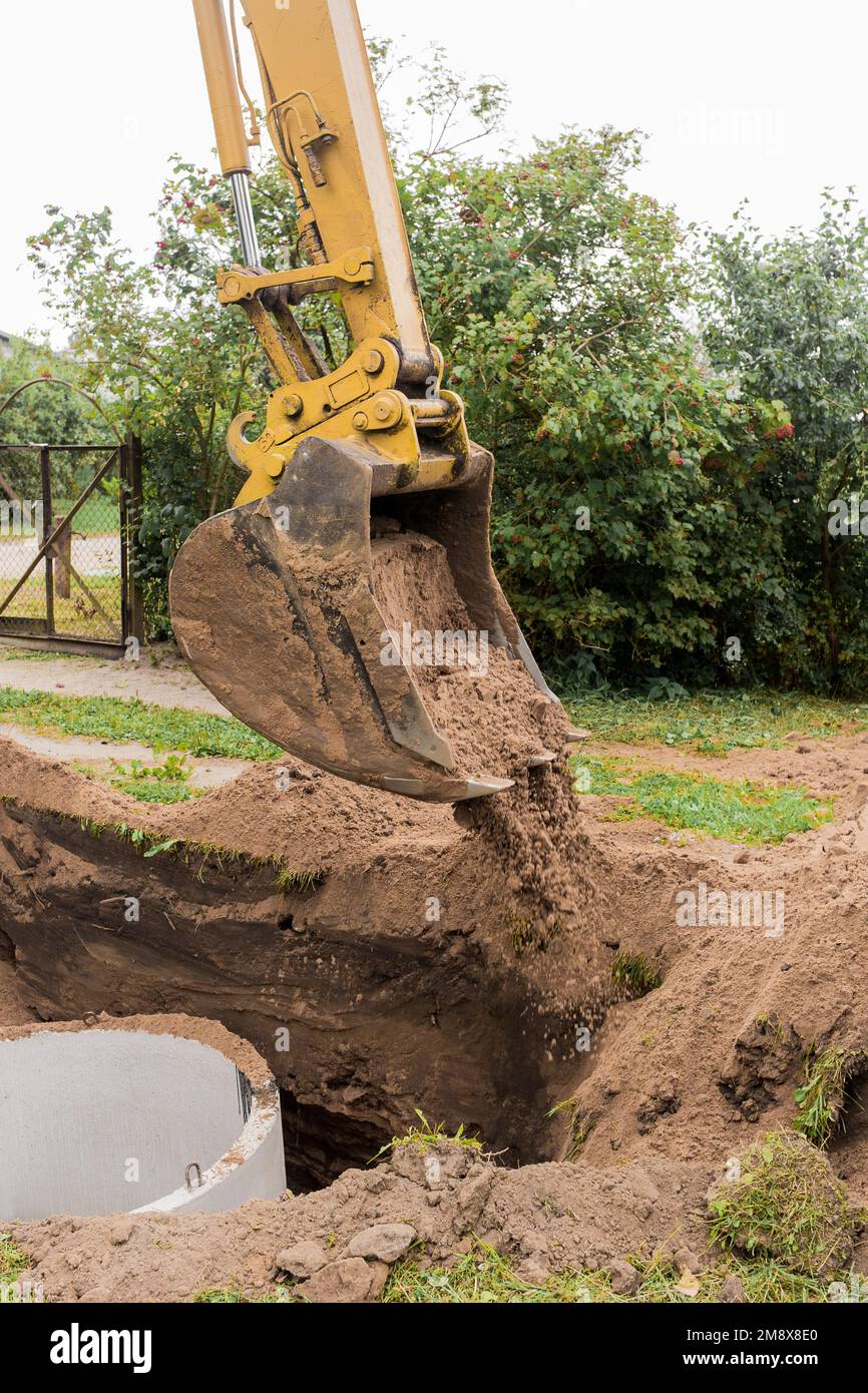 Ein Eimer Bagger mit einem Haufen Sand und Erde begräbt Kanalisation Betonringe in der Industriezone. Stockfoto