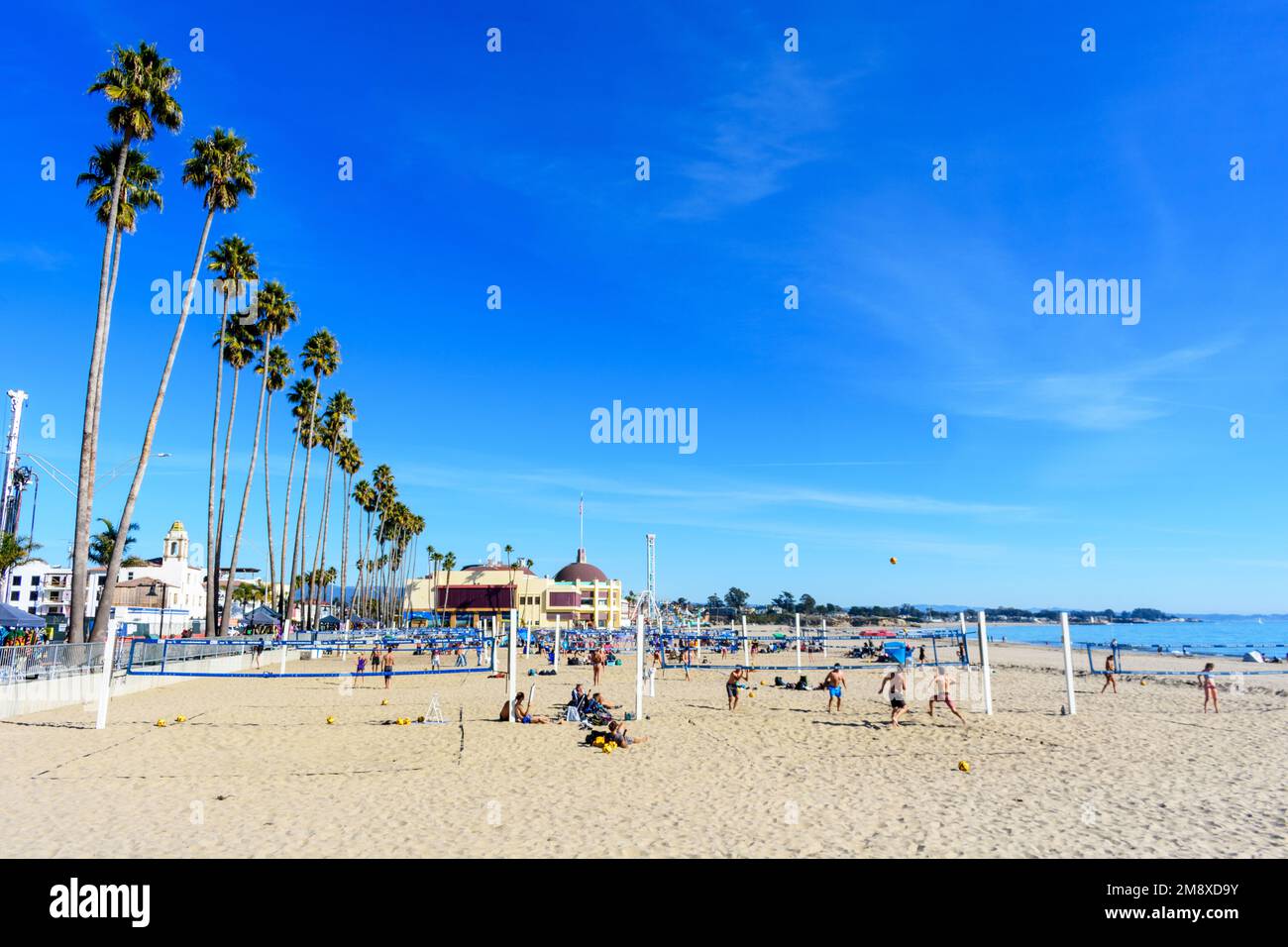 Boardwalk Beach mit Palmen in Reihe, Volleyballplätzen und Menschen. Der Santa Cruz Beach Boardwalk ist im Hintergrund - Santa Cruz, Kalifornien, USA Stockfoto