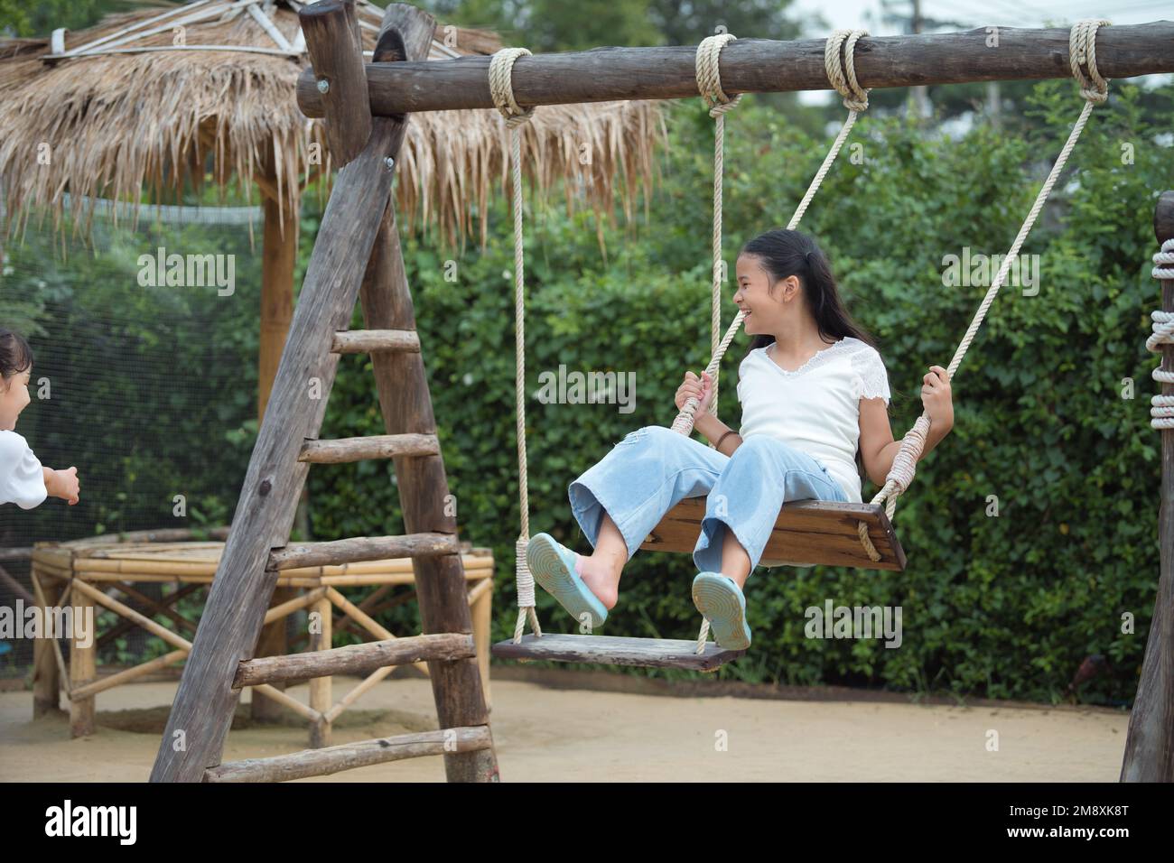 Glückliches Mädchen, das auf der Holzschaukel auf dem Spielplatz spielt. Stockfoto