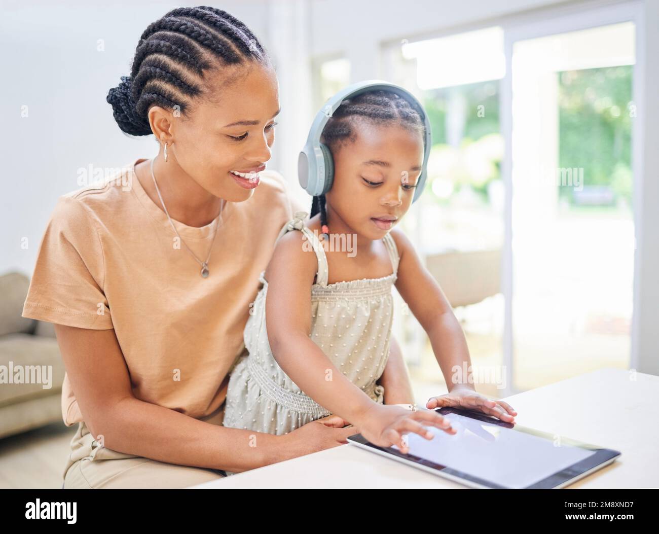 Sie so engagiert wie möglich zu halten. Eine attraktive junge Mutter, die bei ihrer Tochter sitzt und ihr mit einem digitalen Tablet beim Lernen hilft. Stockfoto