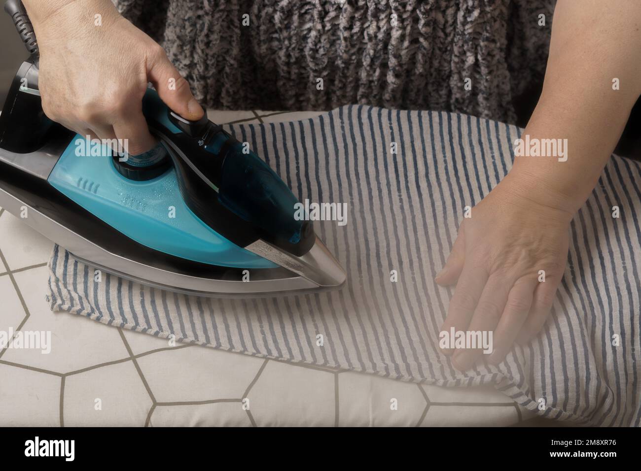 Frau bügelt ein gestreiftes T-Shirt durch Dampfbügeln Stockfoto