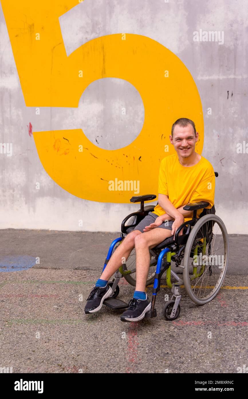 Behinderte Person in einem öffentlichen Park im Rollstuhl, trägt ein gelbes, lächelndes T-Shirt Stockfoto