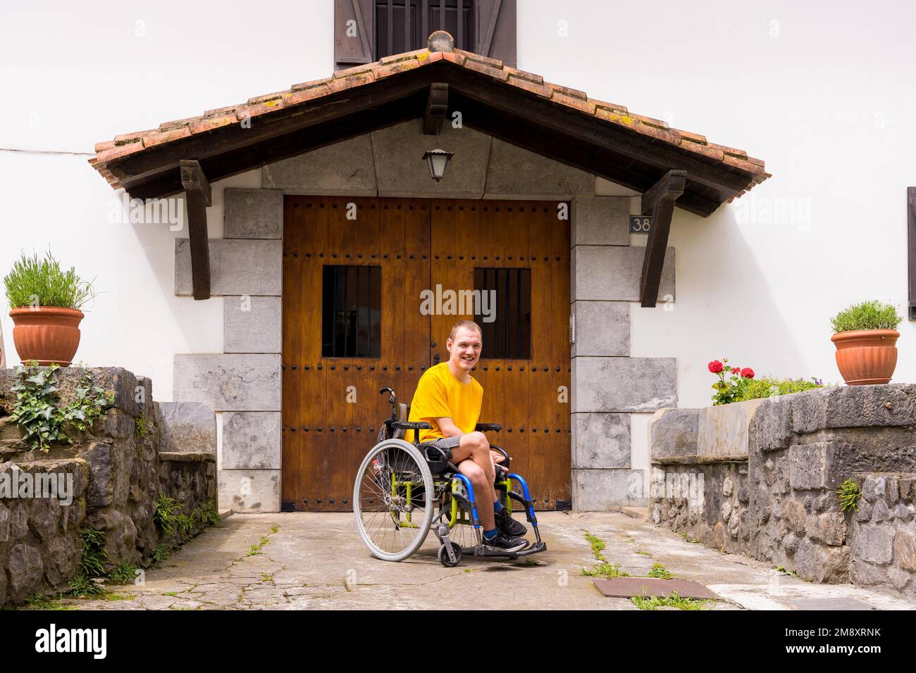 Ein lächelndes Bild eines behinderten Menschen im Rollstuhl am Eingang seines Hauses Stockfoto