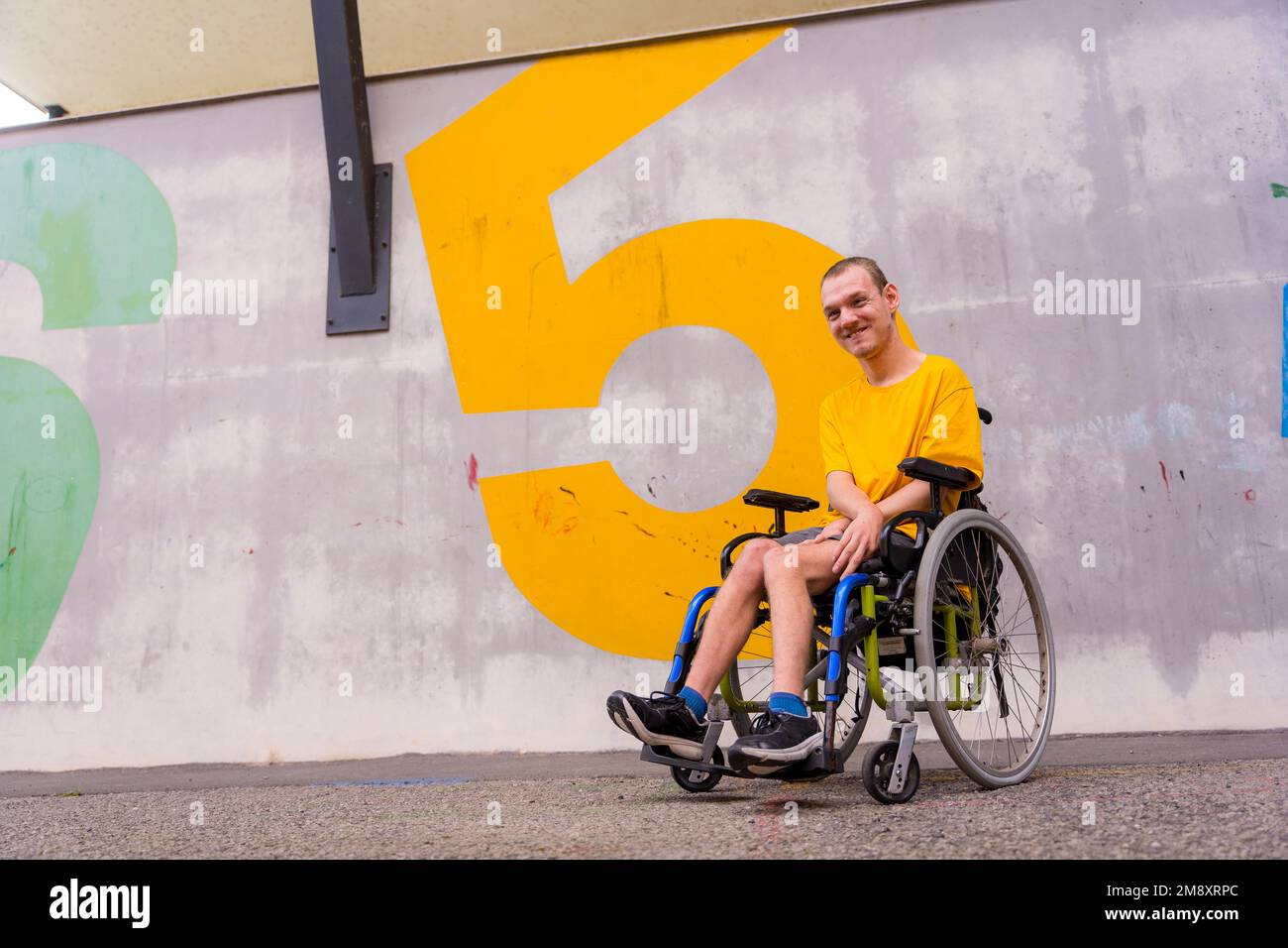 Eine behinderte Person in einem öffentlichen Park im Rollstuhl, die ein gelbes T-Shirt trägt Stockfoto