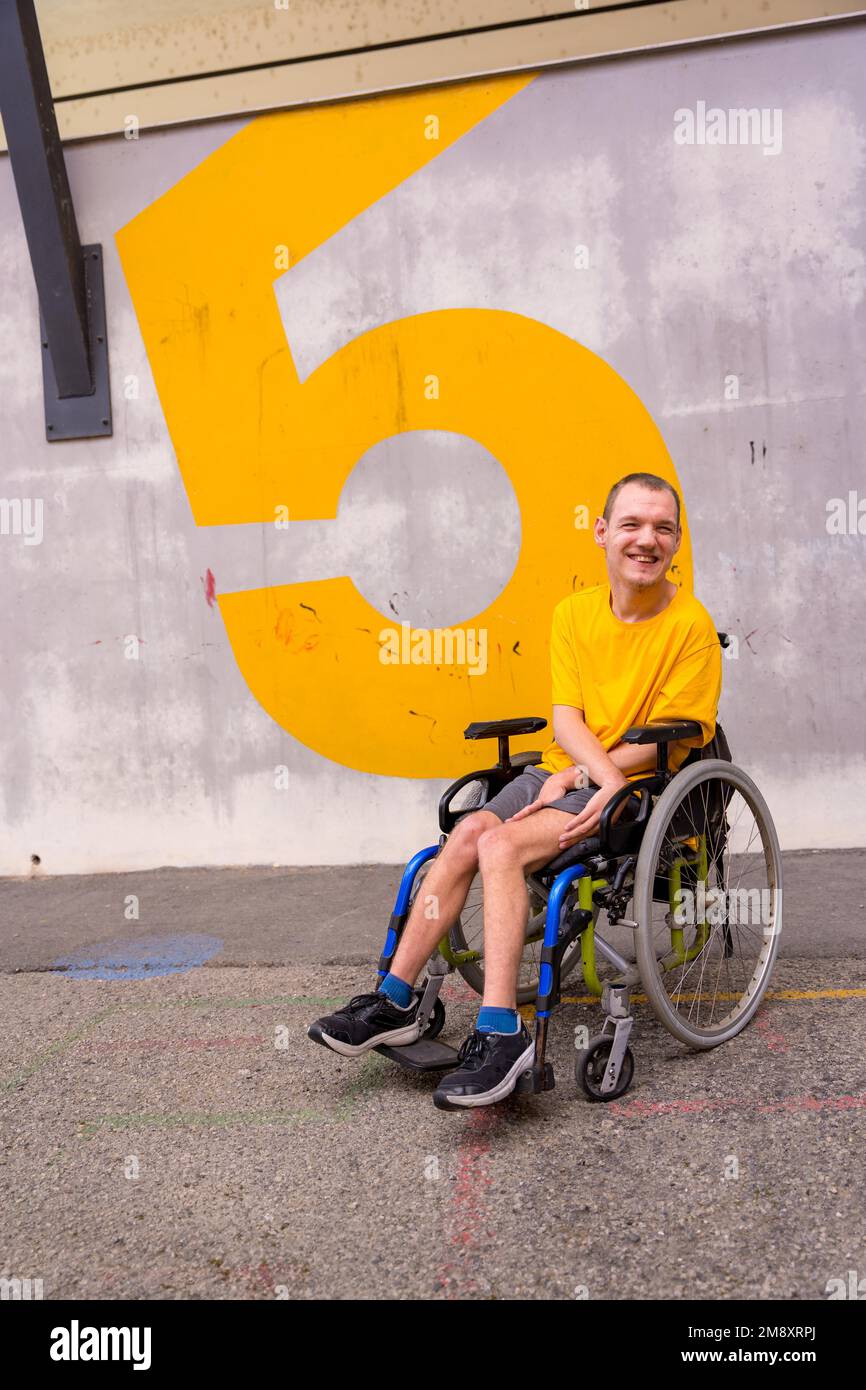 Eine behinderte Person in einem öffentlichen Park im Rollstuhl, die ein gelbes T-Shirt trägt Stockfoto