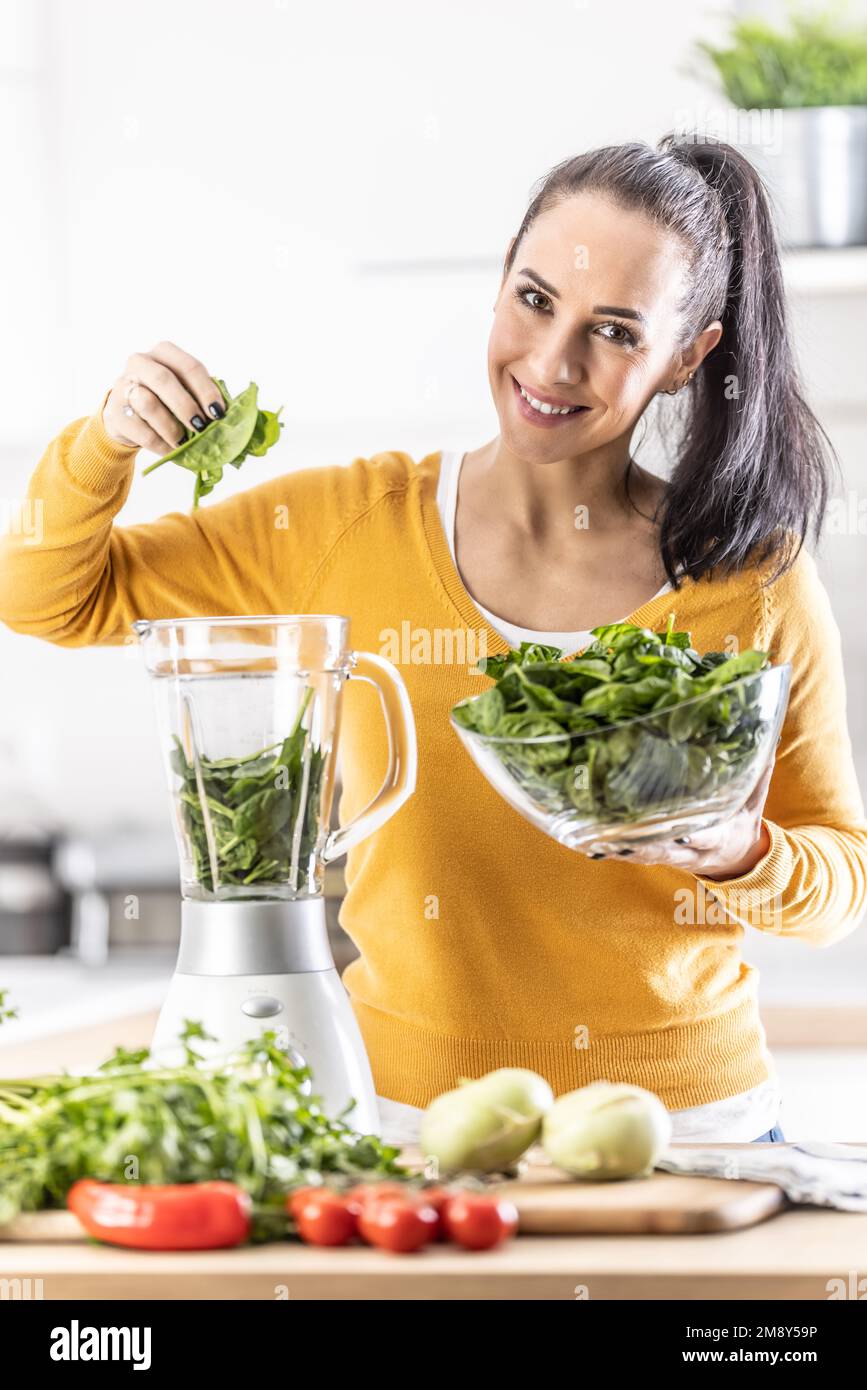 Lächelnde Frau, die Spinat-Smoothie macht, Blätter in den Mixer gibt. Konzept einer gesunden Lebensweise und Ernährung. Stockfoto