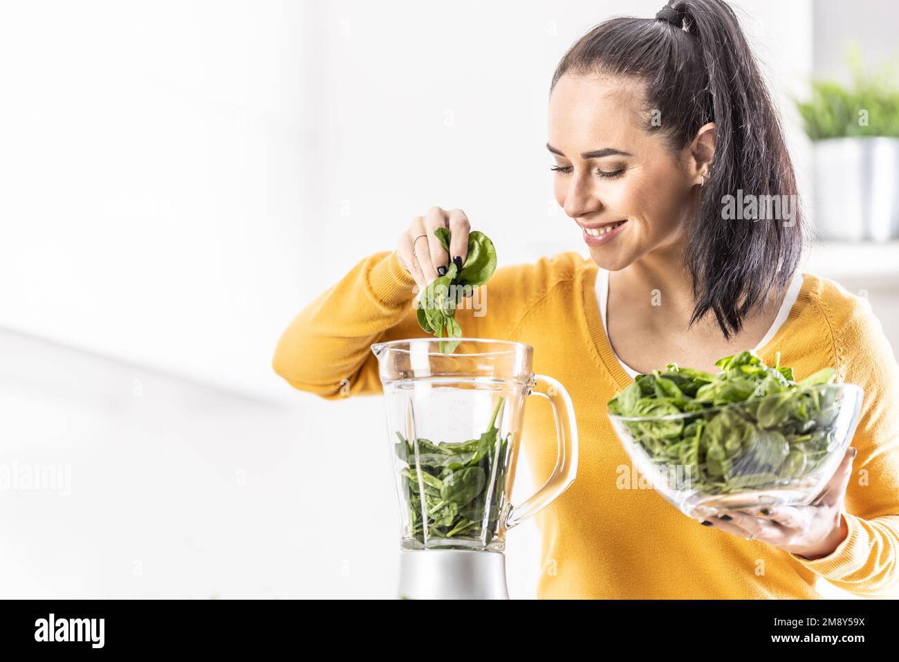 Lächelnde Frau, die Spinat-Smoothie macht, Blätter in den Mixer gibt. Stockfoto