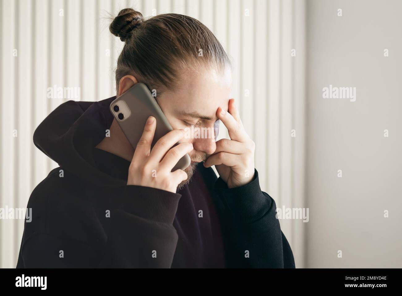 Ein junger Mann, der mit dem Smartphone spricht und seinen Kopf hält, das Konzept des Problems. Stockfoto