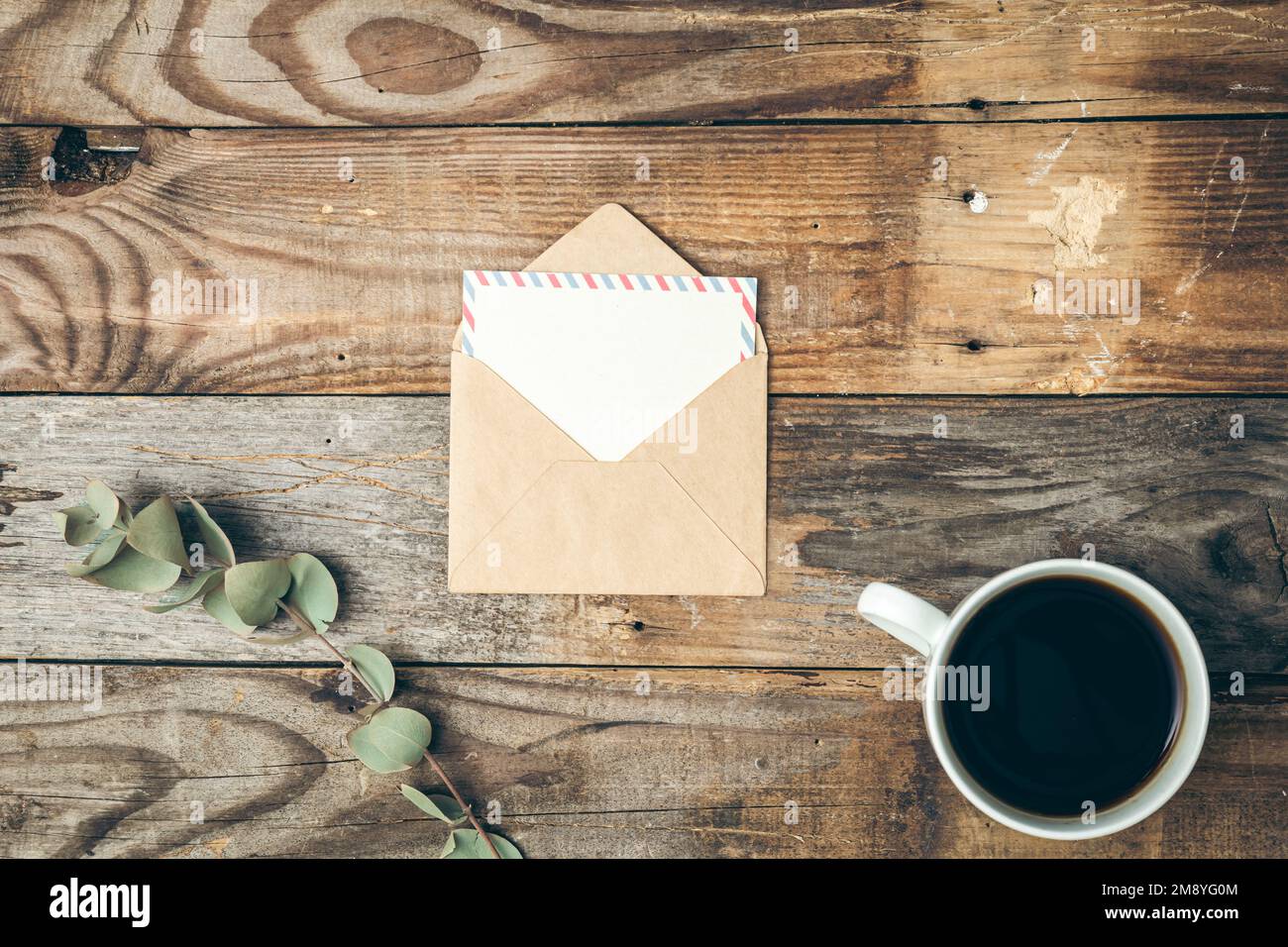 Umschlag, eine Tasse Kaffee und ein Zweig Eukalyptus auf einem hölzernen Hintergrund. Stockfoto