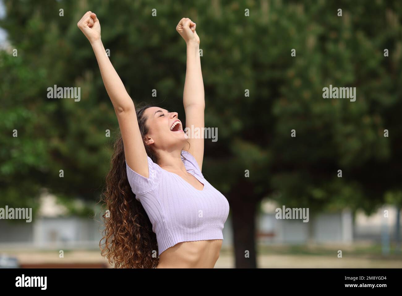 Aufgeregte Frau, die in einem Park die Arme erhebt, um den Erfolg zu feiern Stockfoto