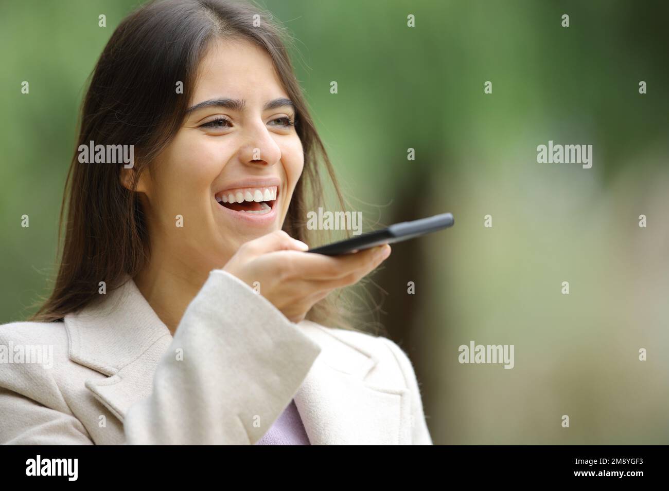 Glückliche Frau, die im Winter Spracherkennung mit Smartphone verwendet Stockfoto